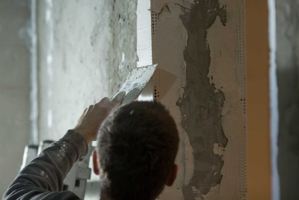 Man plastering a wall | Featured image for the blog How to Panel a Wall from BetaBoard.