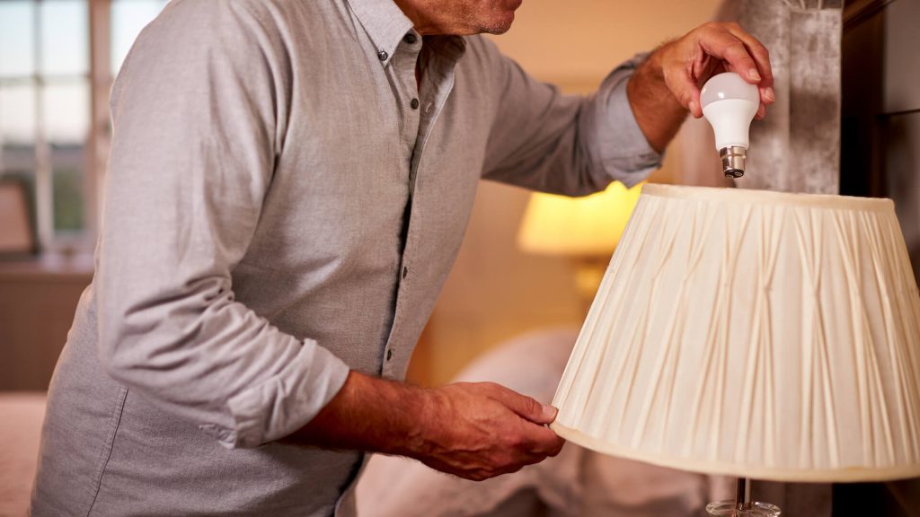 Man installing an LED light bulb in a lamp | Featured image for How to Make Your Home More Energy Efficient blog from BetaBoard.