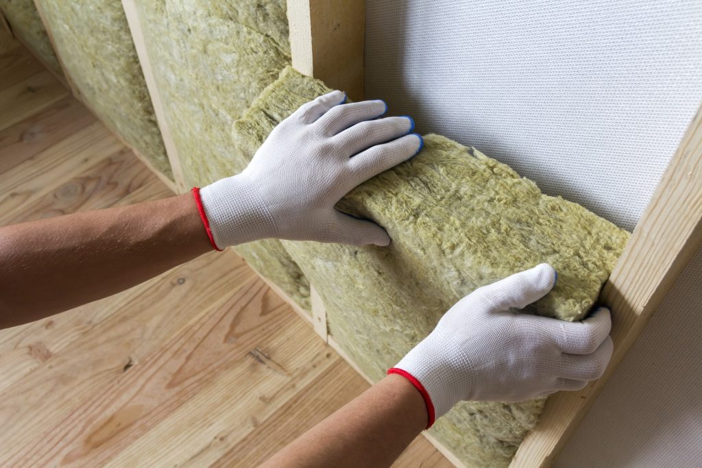 A worker installing insulation | Featured image for the Benefits of Insulating Your Home blog from BetaBoard.