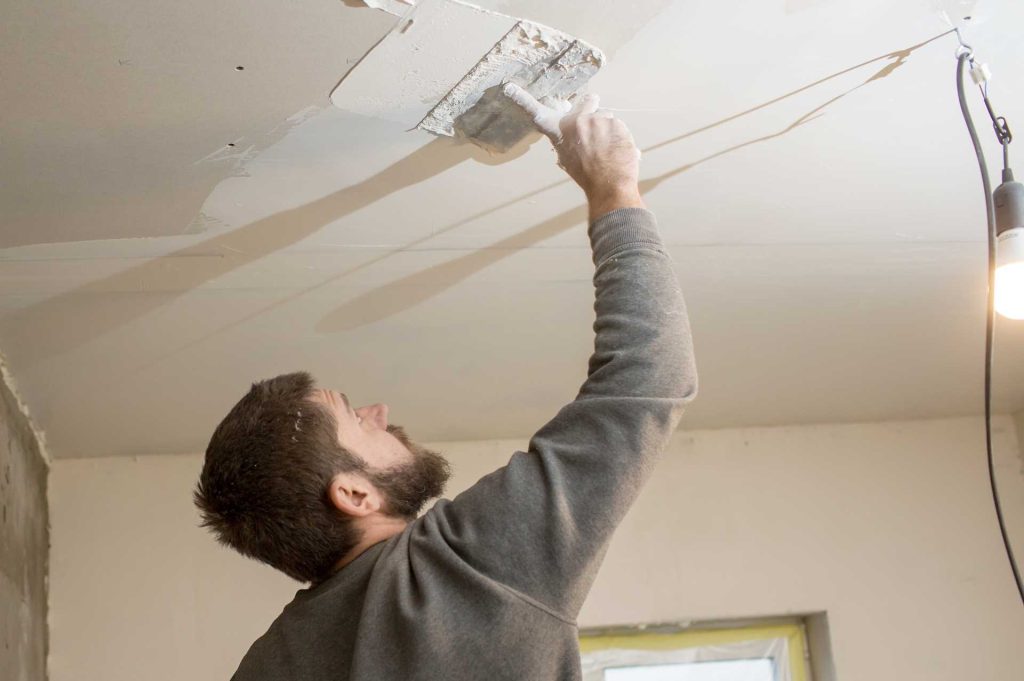 Man plastering a ceiling | Featured image for the How to Plaster a ceiling blog from BetaBoard.