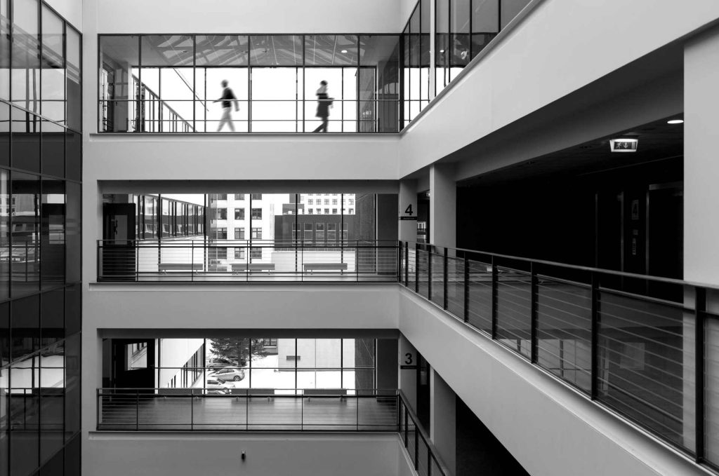 Two people walking on open walkways in a modern building | Featured image for the Architectural Design Trends 2024 blog from BetaBoard.